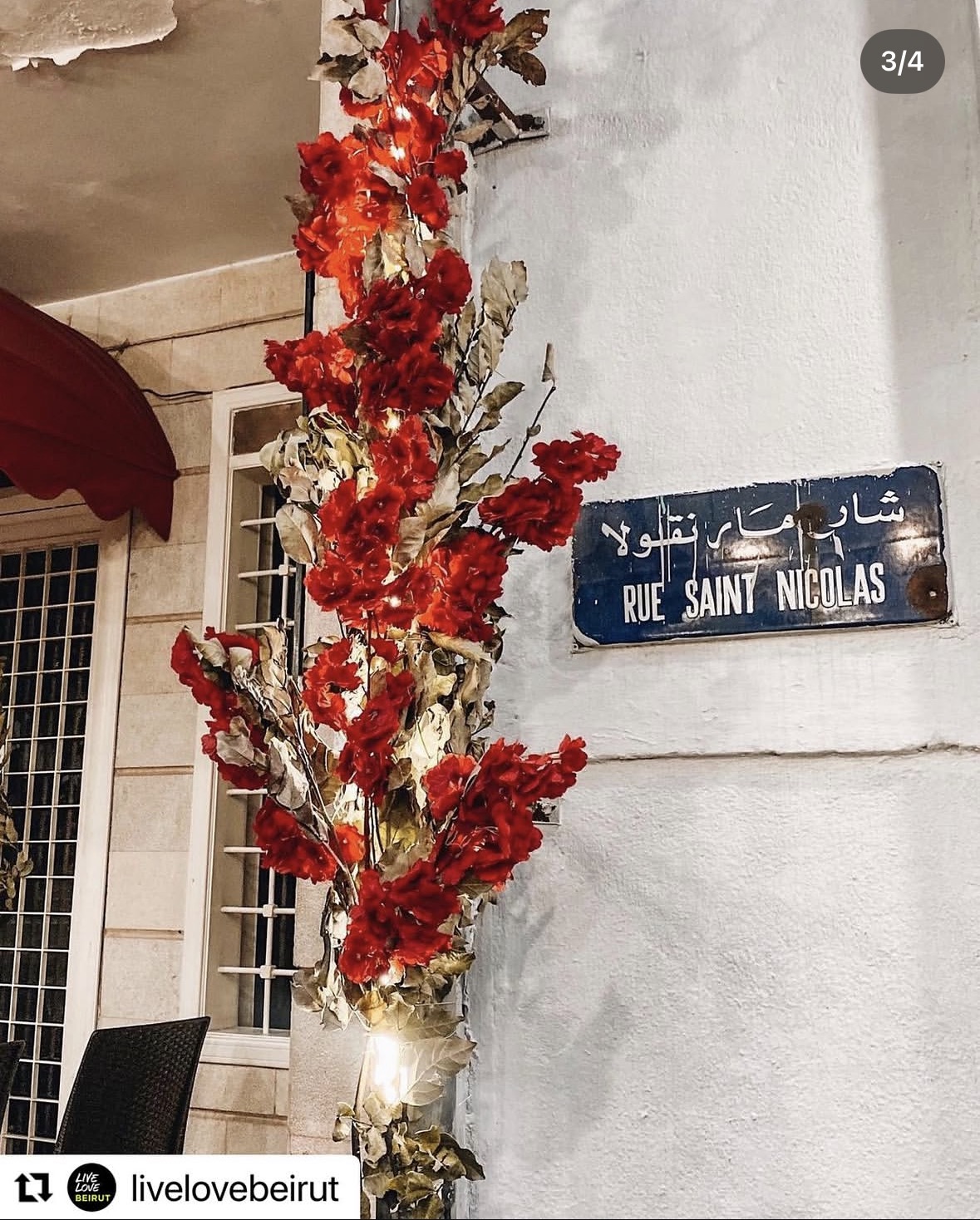 The blue Rue Saint Nicolas street sign beside a column wrapped in red flowers and fairy lights